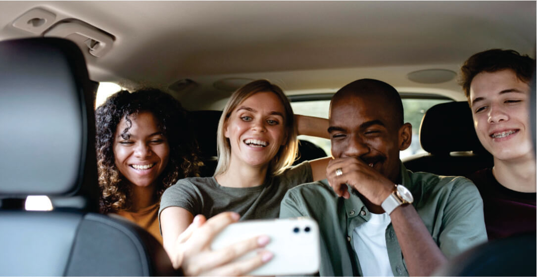 Four friends in a car taking a selfie together on group shuttle safari transfer from Nairobi to Masai Mara.