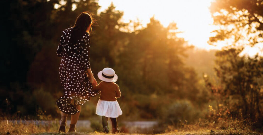 Woman and child walking together in a field at sunset