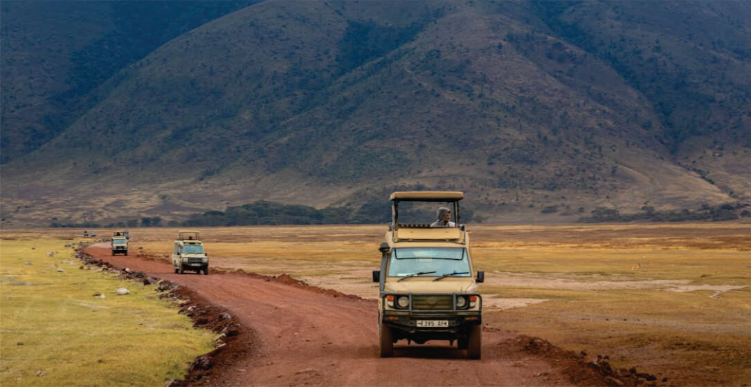 Three safari vehicles on a dirt road with mountains in the background