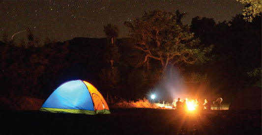 Camping scene with a colorful tent, bonfire, and people around at night.
