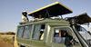 Two women sitting on top of a green open-roofed safari jeep on rental with driver guide
