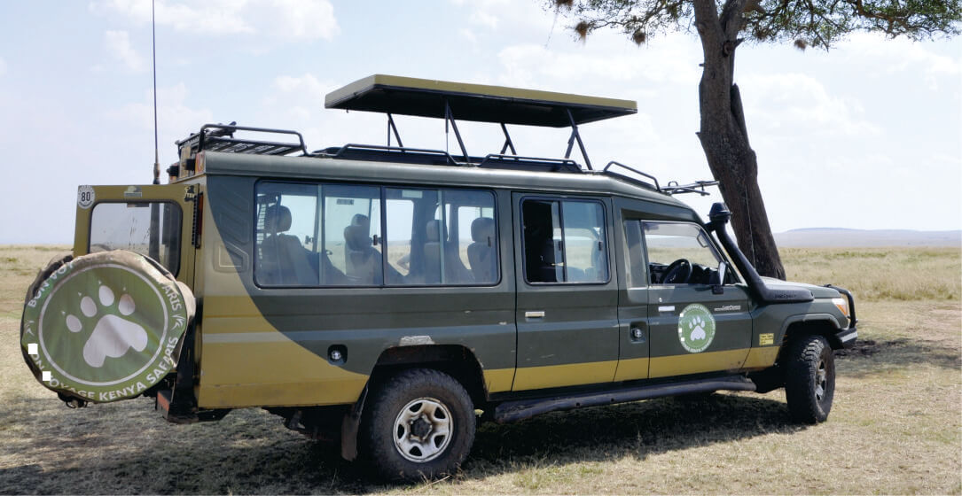 Large green off-road vehicle on rental with a spare tire and an open roof near tree on a savannah in Kenya