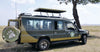 Large green off-road vehicle on rental with a spare tire and an open roof near tree on a savannah in Kenya