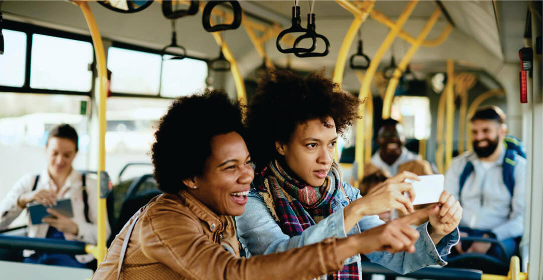 Two people sitting on a bus, looking at a phone together on group shuttle bus safari transfer from Nairobi to Masai Mara.