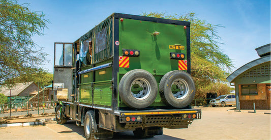 Green truck for Ol Pejeta Conservancy safari vehicle rentals with large wheels on a dirt road with trees and buildings in the background