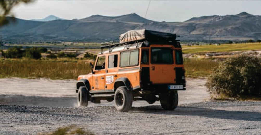 Orange off-road vehicle with a roof rack on a dirt road with mountains in the background