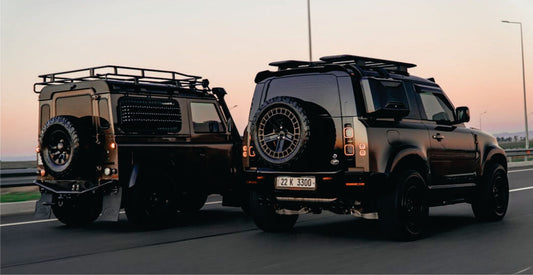 Two black off-road vehicles transfer from Nairobi to Amboseli National Park Safari on a road with a sunset sky.