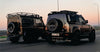 Two black off-road vehicles transfer from Nairobi to Amboseli National Park Safari on a road with a sunset sky.