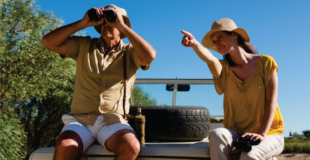 A guide and a woman on a safari, one using binoculars and the woman pointing, with a Samburu Kenya Safari game drive vehicle rental and tire in the background.