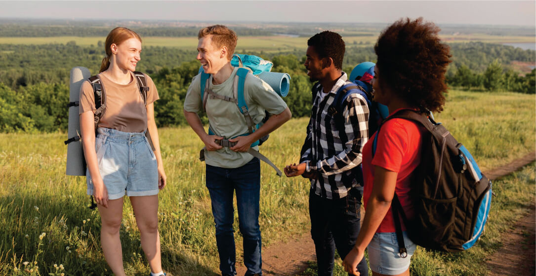 Four friends with backpacks standing in a grassy field with a scenic background on small group budget safari game drives in Masai Mara