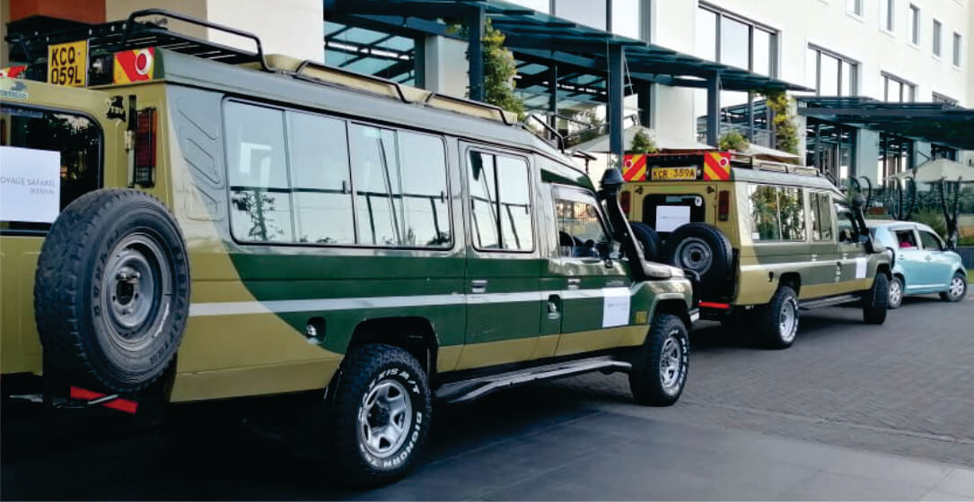 Two green and beige 4x4 jeep safari vehicles parked at a Nairobi city Hotel, awaiting transfer from Nairobi to Samburu Kenya Safari