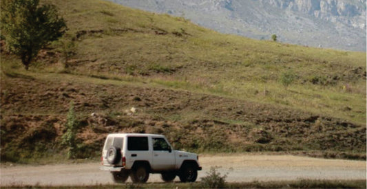 White transfer SUV on a dirt road with green hills and mountains in the background for comfortable Nairobi Samburu safari transport option