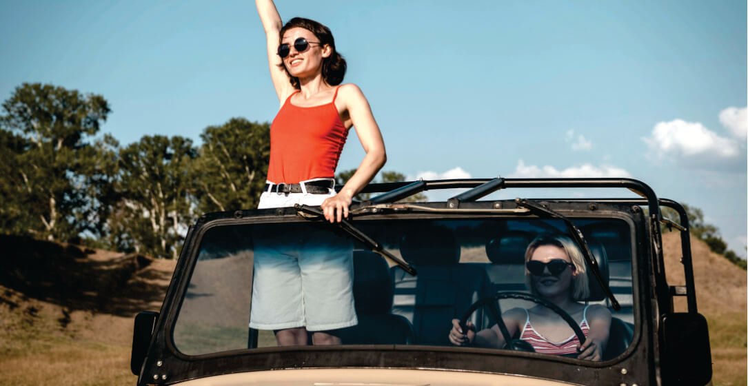 Woman in red top standing on an open safari jeep with a scenic background
