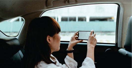 Person sitting in a transfer car holding a smartphone with a blurred outdoor background on transfer from Nairobi to Amboseli National Park Safari