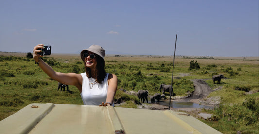 Woman taking a selfie with elephants in the background on a safari vehicle on solo joining safari game drives in Masai Mara.