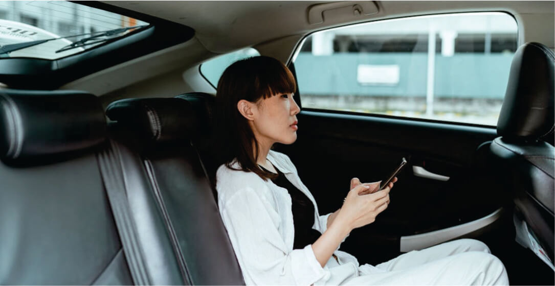 Woman sitting in a transfer car, looking at her phone with a blurred background